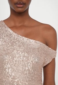 Gros plan d'une femme portant une robe asymétrique rose pâle à sequins avec une épaule droite et un décolleté nus.