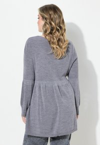 Sweater en tricot gris avec une coupe décontractée, texture côtelée, manches longues et ourlet évasé. La vue arrière montre les détails de style et de tissu.