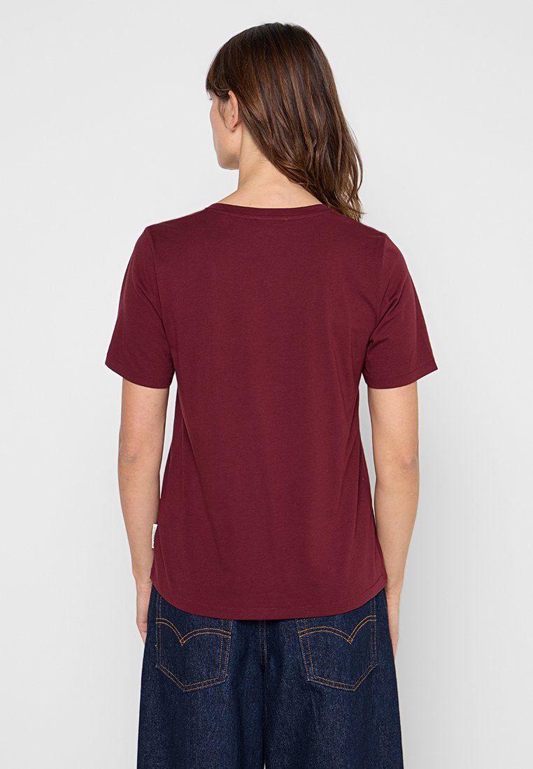 Bordowa koszulka z okrągłym dekoltem i krótkimi rękawami, wykonana z gładkiego materiału. Z tyłu widoczny jest subtelnie zaokrąglony dół.