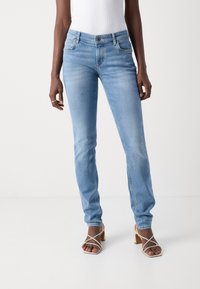 Jeans in denim blu chiaro con vestibilità slim, design a cinque tasche e chiusura con bottone, abbinati a sandali con tacco alto beige e cinturini.