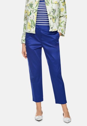 Woman wearing blue cropped pants, white pointed flats, blue and white striped top, and a white jacket with yellow lemon print.