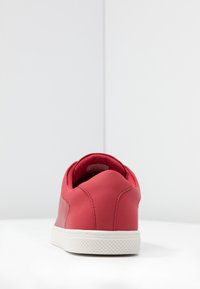 Baskets rouges avec une tige en caoutchouc lisse, détails perforés, col rembourré et semelle blanche texturée. Design minimaliste et forme élégante.