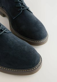 Chaussures en daim bleu marine à bouts ronds, dotées de lacets et d'une semelle contrastée cousue. La surface semble douce et texturée.