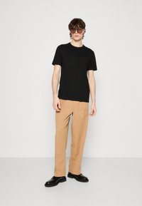 Čierne tričko s krátkymi rukávmi, okrúhlym výstrihom, v kombinácii s béžovými nohavicami a čiernou obuvou, s voľným strihom a hladkou textúrou.