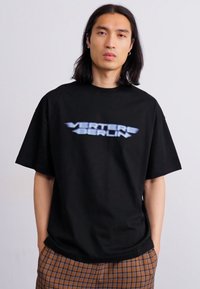 Czarny, luźny t-shirt wykonany z bawełny, z wyraźnym białym napisem "VERTERE BERLIN" z delikatnym efektem gradientu na piersi.