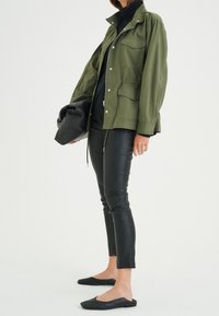 Olive green lightweight jacket with front pockets, paired with black leather skinny pants and black slip-on flats. Simple, functional design.
