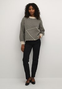 Pull rayé crème et noir avec une coupe boxy, des poignets côtelés et un motif diagonal, associé à un pantalon slim noir et des chaussures noires.