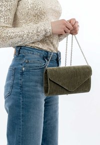 Clutch in verde oliva, con texture, design a pieghe e tracolla in argento, tenuta da una persona che indossa un top con paillettes e jeans.