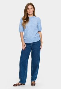 Hellblaues, kurzärmliges Strickoberteil mit geripptem Saum, kombiniert mit weit geschnittenen blauen Jeans. Getragen mit Ballerinas im Leopardenmuster.
