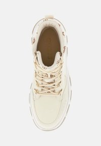 Zapatilla de color crema con parte superior de cuero suave, ojales de hardware dorado y un patrón texturizado en el cuello del tobillo. Interior acolchado.