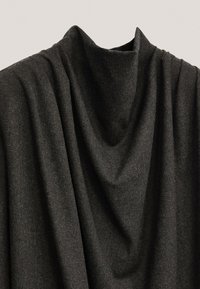 Tissu gris foncé texturé drapé en plis doux, présentant un col haut drapé. Le matériau semble chaud et épais, suggérant une grande durabilité.