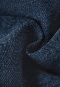 Dunkelblaue Denimstoffe mit glatter Textur, die einen leichten Glanz und subtile Farbvariationen aufweisen, in eine fließende Form gedreht.