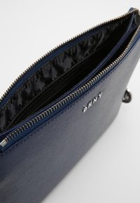 Granatowa kopertówka na zamek wykonana z fakturowanego materiału, z wzorzystą czarną podszewką oraz małym metalowym logo.