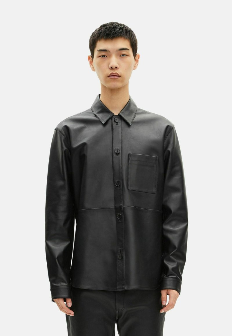 Camicia in pelle nera con design a bottoni, colletto a punta e tasca sul petto. Presenta una superficie liscia e una vestibilità su misura.