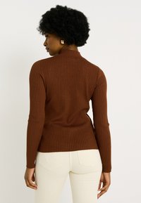 Pull en rib avec col montant et manches longues, associé à un pantalon de couleur claire. Texture lisse avec silhouette ajustée.