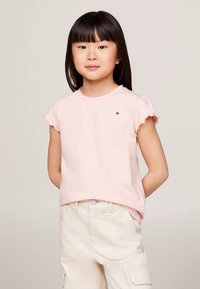 Tricou roz cu mâneci scurte, margini cu volane și un mic logo pe partea stângă a pieptului, asortat cu pantaloni scurți cargo de culoare bej deschis.