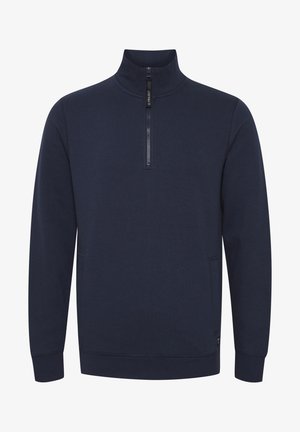 Tumši zilas krāsas džemperis ar augstu apkakli, puscietu priekšu un sānu kabatām. Izgatavots no mīkstas, teksturētas auduma ar brīvu piegriezumu.