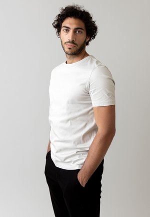 Witte katoenen T-shirt met een ronde hals en korte mouwen, voorzien van een subtiel logo op de linkermouw, gecombineerd met zwarte broek.