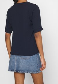 Top blu navy a maniche corte con orli arrotolati, abbinato a una gonna di jeans chiara con tasche e orlo grezzo.