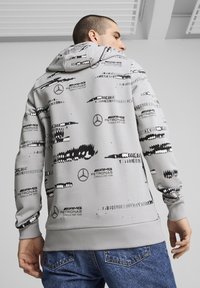 Grey hoodie with black abstract patterns and logos from AMG Petronas Formula One Team. Features a drawstring hood and ribbed cuffs.