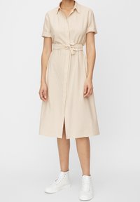 Abito camicia beige a righe con maniche corte e vita legata, con uno spacco frontale. Indossato con sneakers bianche alte.