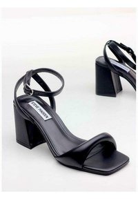 Sandali neri con tacco alto e punta quadrata, realizzati in pelle liscia. Presentano una fascia alla caviglia e un tacco a blocco spesso. Marca: Steve Madden.