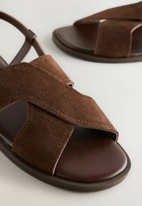 Braune Wildledersandalen mit überkreuzten Riemen, offener Zehenpartie und glattem Lederfußbett. Mit einer robusten braunen Sohle für Komfort und Stabilität.