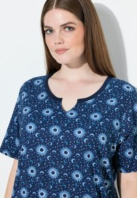 Tmavě modrá košile s krátkými rukávy a výstřihem ve tvaru klíčové dírky, zdobená vzory slunce a měsíce v různých odstínech modré a bílé.