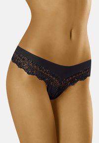 String in pizzo nero caratterizzato da intricati motivi floreali e dettagli trasparenti. Tessuto morbido nella parte anteriore, che contrasta con il pizzo testurizzato sui bordi.