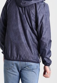 Marinblå huva jacka med texturerad finish, elastisk nederkant, sidofickor och avspänd passform, kombinerad med ljusblå jeans.