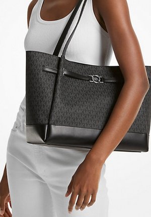Bolso tote grande de lona negra con un patrón geométrico, que presenta un logo plateado brillante y detalles de cuero. Correas de hombro ajustables.
