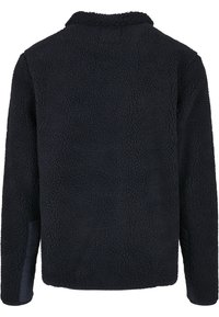 Mustast fliisist jakk tekstuurse, pehme pinnaga. Omaduseks pikad varrukad ja kraega disain, sobib soojuse ja mugavuse tagamiseks.