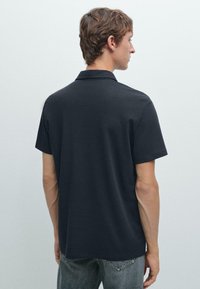 Marinblå polo med klassisk krage, korta ärmar och rak passform. Slät tygtextur utan synliga mönster eller detaljer.