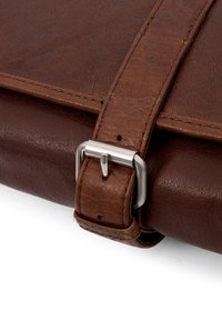 Brown leather bag close-up, featuring a textured surface, strap with a silver metal buckle, and visible stitching detail.