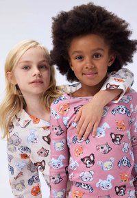Kaksi lasta, jotka pojalla on yllään eläinkuosilla varustetut pyjamat. Toinen paita on kerma, jossa on värikkäitä eläin kasvoja; toinen on vaaleanpunainen, ja siinä on samanlainen muotoilu.