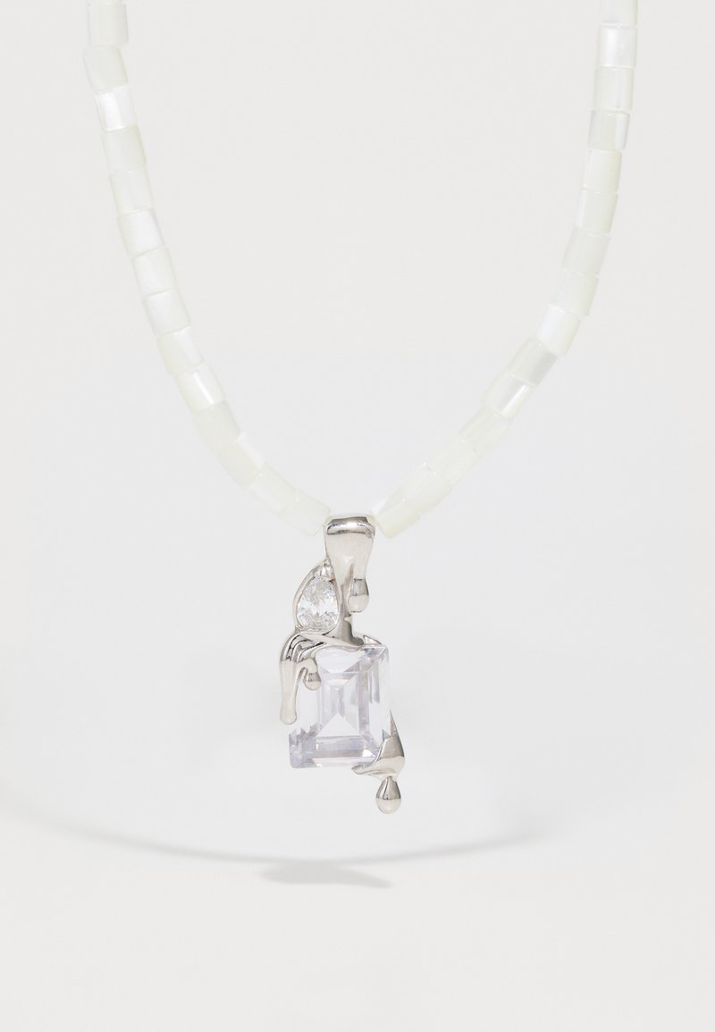 Violeto kristāla piekariņš uz sudraba ķēdītes, ar caurspīdīgu asaras formas akcentu un kvadrātveida dizainu, kas rotāts ar gaišas krāsas kvadrātveida pērlītēm.