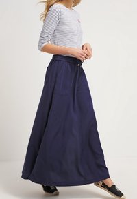 Marinblå, följsam maxikjol med elastiskt midjeband och två sidfickor, tillsammans med en vit och marinrandig långärmad topp.