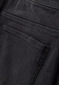 Musta denimkangas, jossa on sileä pinta. Sisältää takataskun, jossa on yläommeltu yksityiskohta ja hienovaraisia kulumisjälkiä, mikä korostaa nykyaikaista muotoilua.