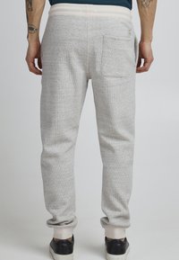 Joggers de felpa gris claro con un patrón texturizado, cintura elástica y puños acanalados. Presenta un bolsillo trasero y detalles de costura sutiles.