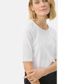 Balta trumpa rankovė t-shirt marškinių su apvalia iškirpte, pagaminta iš lygaus medvilninio audinio, pasižyminti laisvu siluetu ir minimaliais dizaino akcentais.