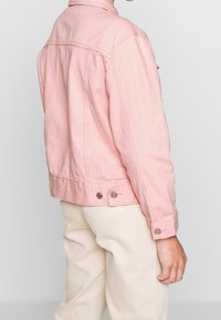 Rosa denimjacka med en klassisk design, som har krage, tryckknappar och en lätt blekt textur.