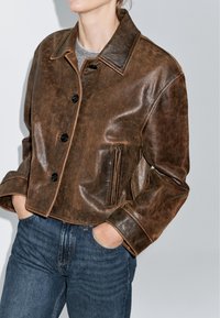 Bruine leren cropped jas met een klassieke kraag, knopenpand en zijzakken. Heeft een gladde textuur en contrasterende stiksels.