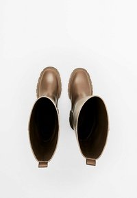 Een paar hoge, bruine rubberen laarzen met profielzolen, van bovenaf bekeken op een witte achtergrond.