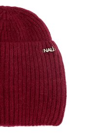Hnědá pletená čepice s ribovanou texturou a ohrnutým lemem. Na boku se nachází stříbrný logový akcent. Měkký materiál směsi vlny.