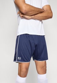 Tamsiai mėlyni sportiniai šortai iš lengvos, orui pralaidžios medžiagos, su baltomis šoninėmis juostelėmis ir balto logotipo žemiau kairės kojos.