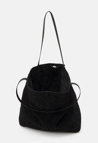 Zwarte suède handtas met een open bovenkant, voorzien van een enkele lange schouderband en een ronde leren accent aan de zijkant. Zachte textuur met minimale naden.
