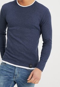 Camicia a maniche lunghe di colore blu navy con un collo bianco a contrasto e un tessuto testurizzato. Include una piccola etichetta con logo nero sull'orlo.
