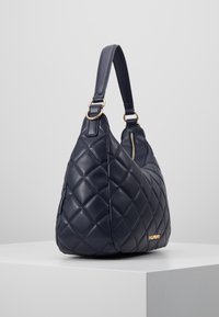 Quiltad marinblå läderhandväska med en böjd design, guldaccessoarer och en enda axelrem, med en dragkedjeslutsats.