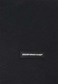 Černý pletený svetr s kulatým výstřihem, který má na hrudi obdélníkovou černou nášivku s bílým textem "GOODFORNOTHING". Hladká textura.