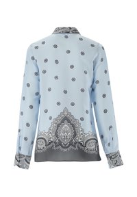 Blusa azzurra chiara con motivi floreali e paisley neri, maniche lunghe e un colletto decorato. Tessuto morbido e uniforme.